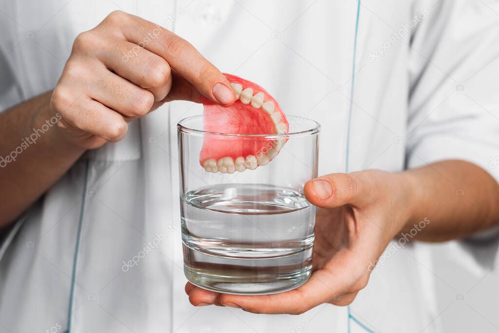 The prosthesis is in a glass with a solution. Dental prosthesis care. Full removable plastic prosthetic jaw. Acrylic denture. A jaw with artificial teeth. Dentures or false teeth close-up