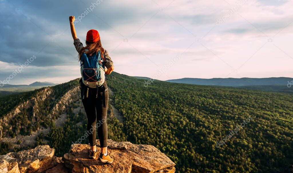 A traveler with a backpack in the mountains at sunset. A traveler with a backpack on the background of mountains, rear view. Hiking trips. A tourist girl on the background of a mountain landscape