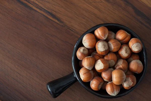 Hazel nuts in black bowl on wooden table — Stock Photo, Image