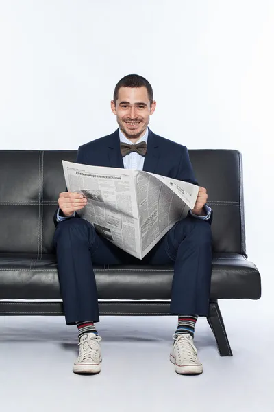 Young man with newspaper sitting on sofa at office — Stock Photo, Image