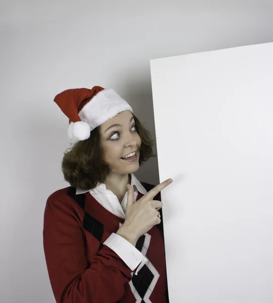 Pretty young woman wearing Santa hat and holding blank sign — Stock Photo, Image