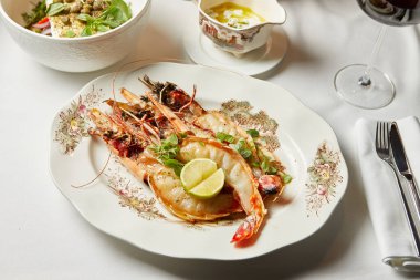 Limonlu ve yeşillikli büyük karidesler bir restoranda akşam yemeği sırasında beyaz tabakta.
