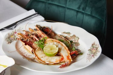 Limonlu ve yeşillikli büyük karidesler bir restoranda akşam yemeği sırasında beyaz tabakta.