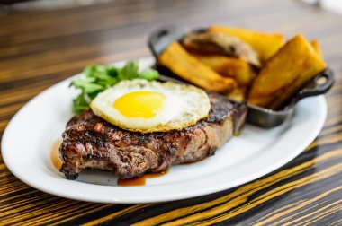 Izgara biftek, patates kızartması, kızarmış yumurta ve sebze. 