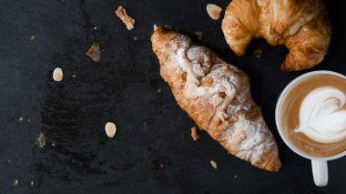Kayrak taşı üzerine taze kruvasan ve latte kahve. Arka planda karanlık bir ruh hali ve ürününüz için kopyalama alanı. en üstteki görünüm