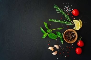 spicy green herbs as ingredients for cooking, consisting of red, black, white, pepper seeds, rosemary, basil, lime, tomato and salt on a slate table. food background dark tone top view with copy space