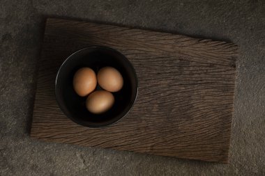 Three raw eggs in a black bowl on the old wooden plank background, top view food still life background with copy space