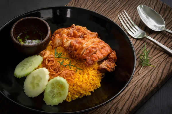 closeup Muslim yellow rice with fried chicken on a black plate with little bowl seasoning on the old wooden plank above the dark kitchen table, halal food top view, Asian food, Thai food cuisine menu