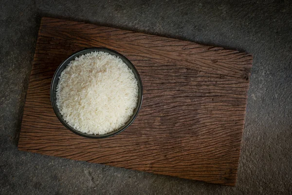 Healthy food. Thai jasmine rice, raw rice in a black bowl above an old wooden plank. Top view, copy space, high-resolution product., still life Thai food top view