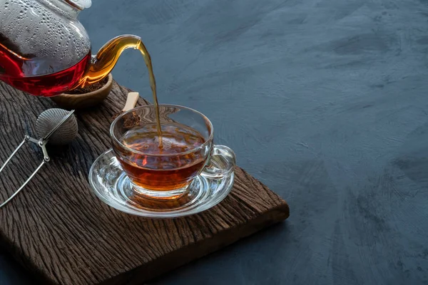 Process brewing tea, Hot tea water is poured from the teapot into a cup on the old wood plank with dark kitchen table background, still life relaxing time dark mood style.
