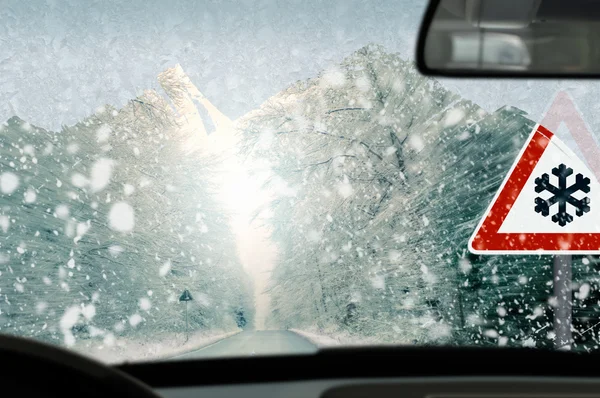 Zimní jízdy - sněžení na silnici s varovným signálem — Stock fotografie