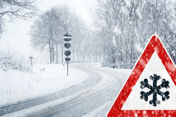 Condução de inverno - queda de neve em uma estrada de país com sinal de aviso — Fotografia de Stock