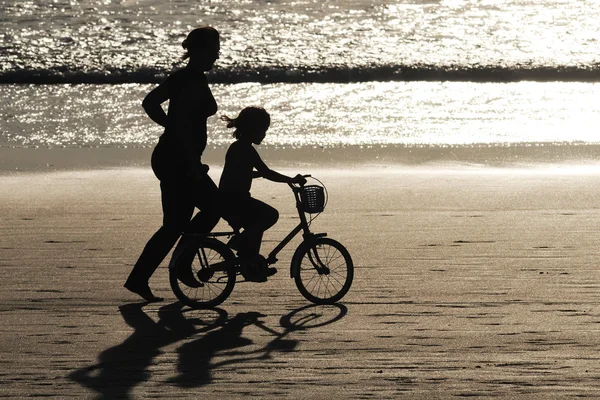 Mädchen lernt Fahrrad mit seiner Mutter am Strand — Stockfoto