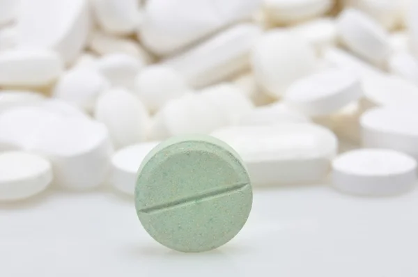 Green tablet among white pills background — Stock Photo, Image