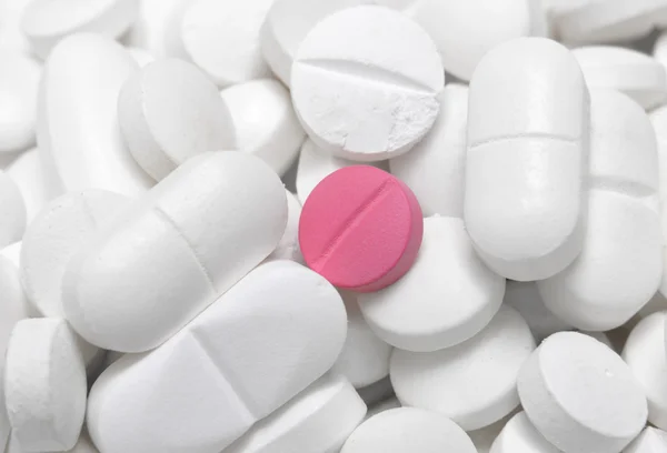 Pink tablet among white pills — Stock Photo, Image