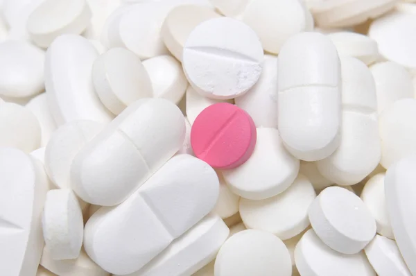 Розовая таблетка среди белых таблеток — стоковое фото