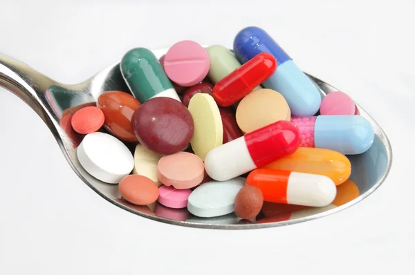 Many different colored tablets and pills on a spoon — Stock Photo, Image