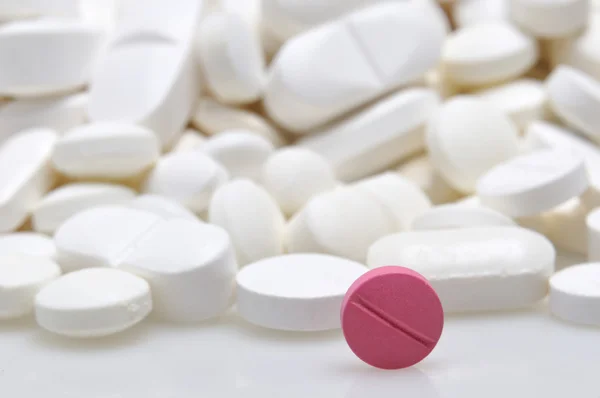 Różowe tabletki wśród tabletki białe tło — Zdjęcie stockowe