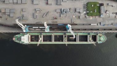 Geminin ambarına yük yükleyen iskele vinçlerinin yukarıdan aşağı hava görüntüsü. Ağır yük taşıyan yeşil gemi. Gemi kargo limanına demirlemiş. Kargo taşımacılığı.