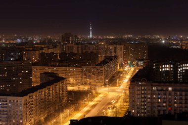 Işıklı fenerlerle ve yüksek konut binalarıyla dolu bir gece fotoğrafı. Arka planda ışıklandırılmış TV kulesi. Büyük şehir hayatı konsepti.