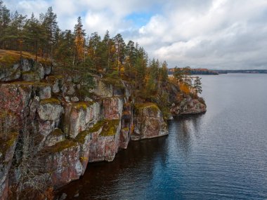 Bitkileri, ağaçları, gölleri ve bulutlu gökyüzü olan kayalık kıyı manzarası. İskandinav doğası, iskarmozlar ve fiyortlar. Sonbahar sezonu. Doğada güzellik. Saf çevre. Viborg, Rusya.