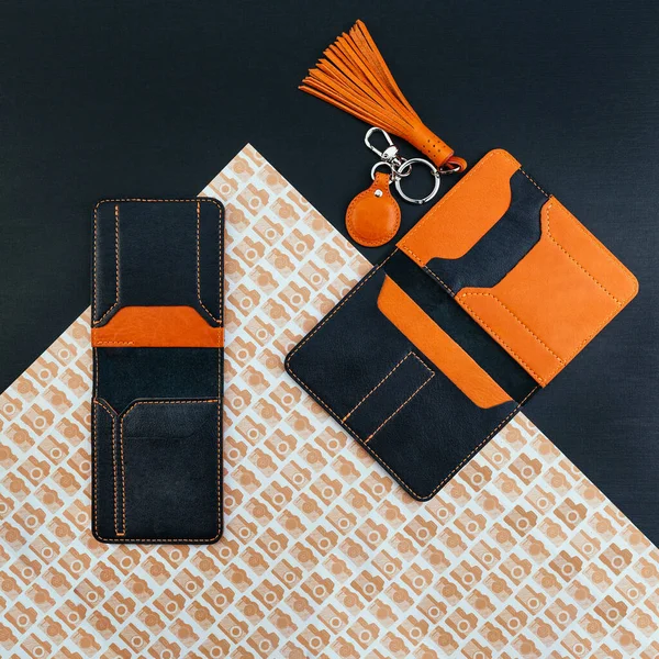 Black and orange stylish leather purse for driver\'s license, passport or id card. Documents cover and holder. Near ginger trinket for keys. Flat lay. Trendy accessories concept. Patterned background.