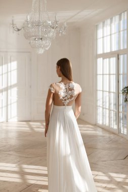 Beyaz gelinlik içinde, tanınmayacak kadar zayıf ve güzel bir kızın dikey fotoğrafı. Gelin evliliğe hazırlanıyor. Ciddi bir olay. Zemin uzunluğunda şık bir gelinlik. Damadı bekliyorum. Doğal güneş ışığı