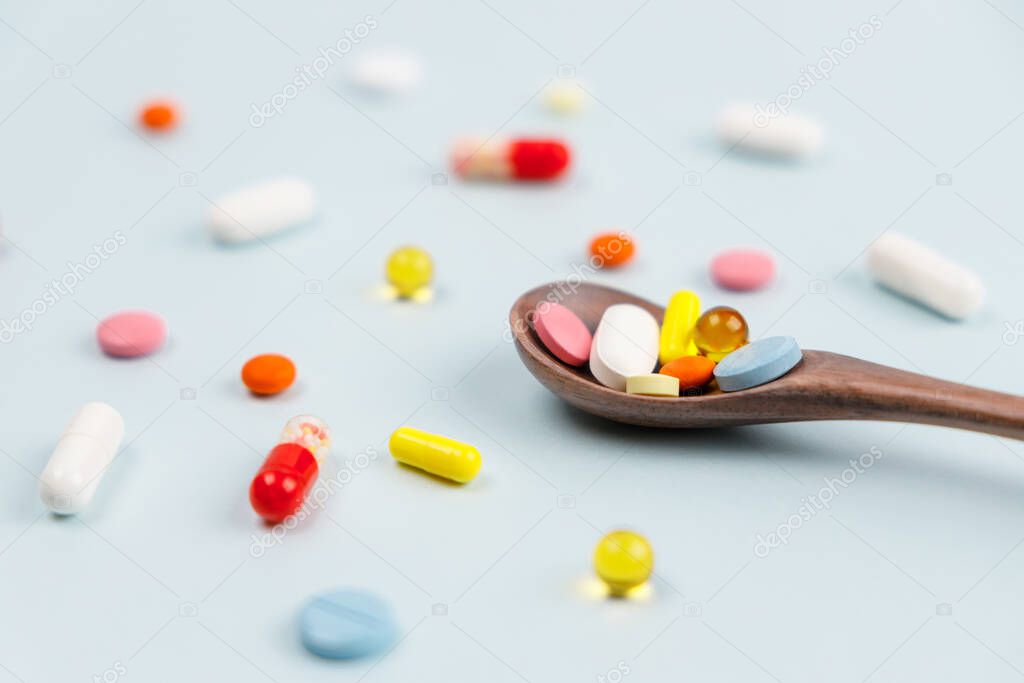 Various colorful multicolored pills on blue background. Tablets in a wooden spoon. Medicines, vitamins, antibiotics and medicaments. Selective focus. First aid treatment and healthcare concept.