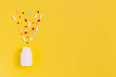 Farklı renklerde haplarla dolu beyaz bir şişe. Hastalık ilaçları: baş ağrısı, boğaz ağrısı, kızarıklık, öksürük, grip veya soğuk algınlığı. Sağlık hizmeti ve sağlık konsepti. Sarı arkaplan, kopyalama alanı. Düz yatıyordu.