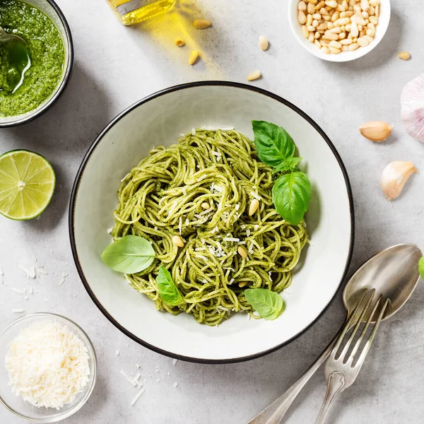 Pesto soslu makarna ve gri kasede taze fesleğen yaprağı. Açık gri arkaplan. Üst manzara..