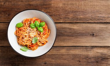 Lezzetli iştah açıcı klasik İtalyan spagettisi domates soslu, parmesan peynirli ve taze fesleğen yapraklı. Ahşap arkaplan, üst manzara
