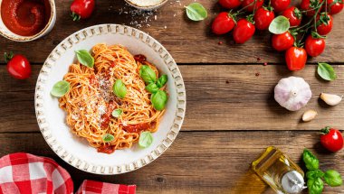 Lezzetli iştah açıcı klasik İtalyan spagettisi domates soslu, parmesan peynirli ve taze fesleğen yapraklı. Ahşap arkaplan, üst manzara