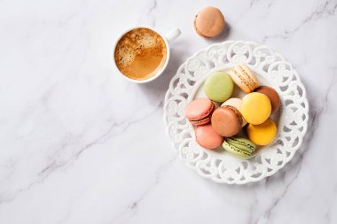 Mermer zemin üzerinde kahve fincanı olan renkli badem kurabiyeleri.