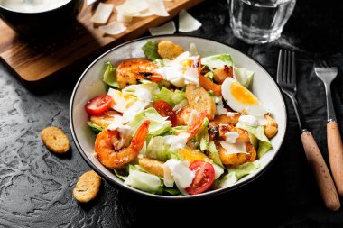 Fresh Shrimp Caesar Salad with parmesan cheese and Croutons. Black stone background.