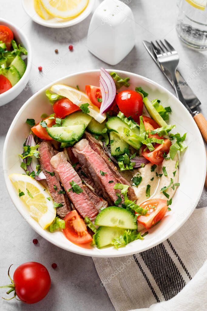 Fresh salad and creamy hummus are topped with  veggies and perfectly grilled steak in this Mediterranean Steak Bowl.