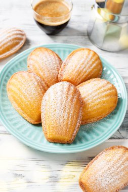 Perfect French madeleine cookies, buttery and delicate, powdered with icing sugar served with cup of coffee. White wooden background. 