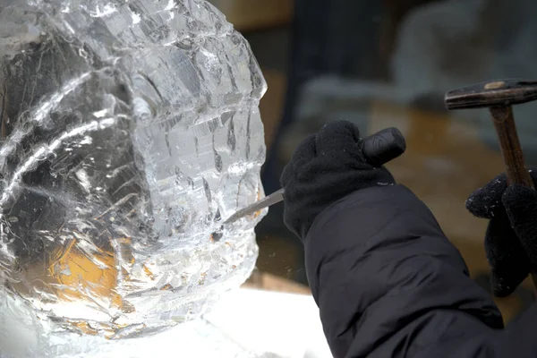 Ice sculptor uses chisel and hammer to chip and work the icy design at an outdoor winter festival.