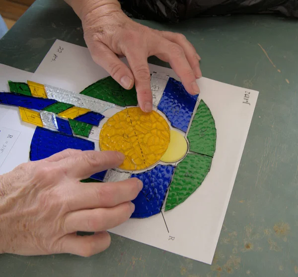 Stained Glass artist checks the cut glass against the design layout.