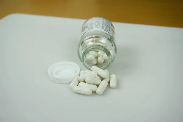 Glass jar and white pharmacy capsules. Administration, use and manufacture of medicines