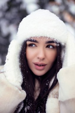 Beyaz kürklü ve beyaz şapkalı uzun saçlı güzel esmer kız otelde eğleniyor. Dış mekan fotoğrafçılığını kapat.