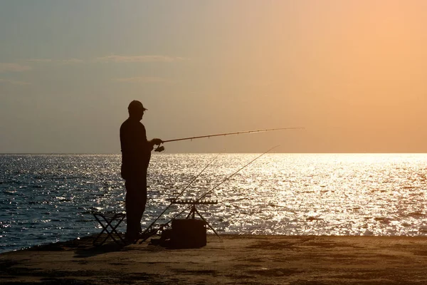 stock image A fisherman is fishing with afishing rod on the seashore, opposite the sun. High quality photo