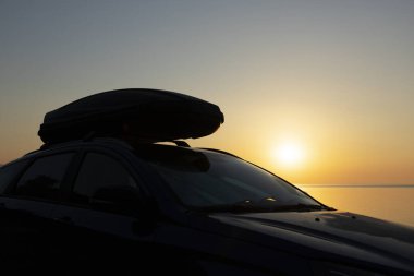 Bagajı kargo kutusu olan bir araba. Denizin üzerinde güneşin doğuşunun arka planında..
