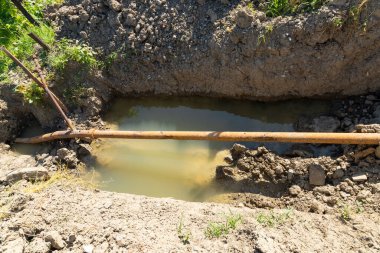 Çukurdaki eski paslı metal borular. Suyu olan bir çukur. Dağlık bir bölgedeki su tedarik sistemi. Paslı bir boru hattının buluşu. Yüksek kalite fotoğraf