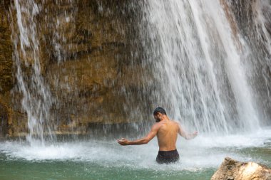 Kollarını kaldırmış beyaz bir adam Avrupa 'da bir dağ nehrinde taze bir şelalenin keyfini çıkarıyor ve banyo yapıyor. Yüksek kalite fotoğraf