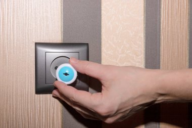 Kahverengi bir duvarda kahverengi bir elektrik prizi ve fişe takan bir kadın eli, çocuk için dayanıklı. Yüksek kalite fotoğraf
