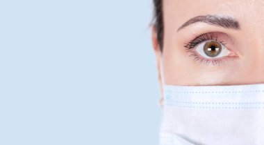 Yakından kahverengi gözlü, delici bir kadın bakışı. Tıbbi maskeli bir kadın doktorun portresi. Tıbbi mavi arka plan. kopyalama alanı. Yüksek kalite fotoğraf