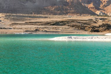 Tuz oluşumlarıyla kaplı kıyıdan Ölü Deniz 'in sularının ötesindeki dağların görüntüsü.
