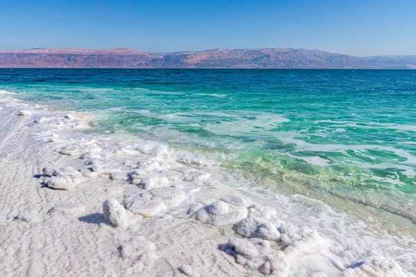 Widok na góry przez wody Morza Martwego od brzegu pokryte formacjami soli. — Zdjęcie stockowe