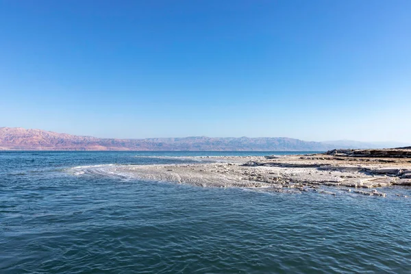 Widok na góry przez wody Morza Martwego od brzegu pokryte formacjami soli. — Zdjęcie stockowe