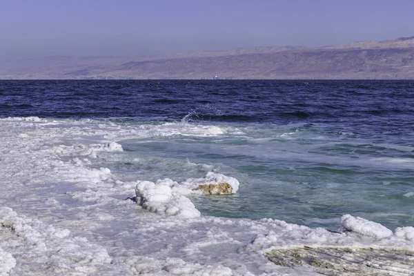 Utsikt över bergen över Döda havets vatten från stranden täckt med saltformationer. — Stockfoto